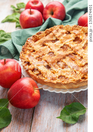 Freshly baked apple pie surrounded by ripe red apples and green leaves on rustic wooden table Freshly baked apple pie surrounded by ripe red apples and green leaves on rustic wooden table 130874401