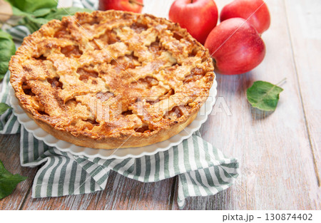Freshly baked apple pie with red apples and leaves on rustic wooden table Freshly baked apple pie with red apples and leaves on rustic wooden table 130874402