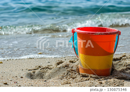 Red and yellow bucket is sitting on the sand at the beach 130875346