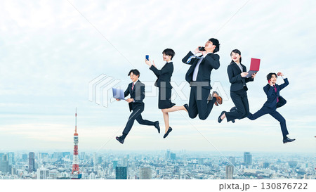 都市を背景にデジタルデバイスを持ってジャンプするビジネスパーソンのグループ 130876722