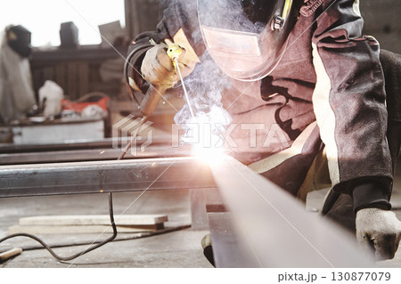 Worker in safety mask welds metal at industrial enterprises. Worker in safety mask welds metal at industrial enterprises. 130877079