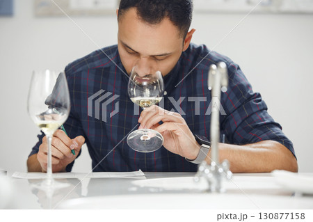 Professional male sommelier smelling and tasting white wine into glass and makes notes to degustation card during sommelier training.  130877158