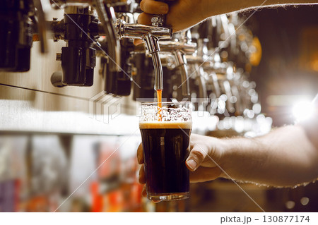 Close up of Bartender Expertly Pouring Stout Beer Into Glass at Busy Bar During Evening Service 130877174