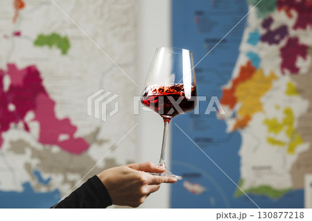 Elegantly Held Red Wine Glass by Faceless Figure Against Map Background 130877218