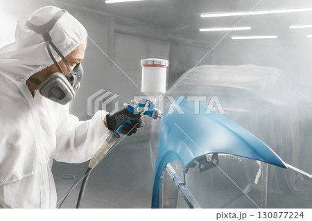 Car repair painter in protective overalls and painting a respirator car wing in the paint chamber 130877224