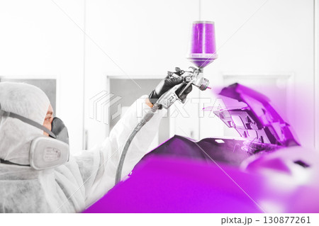 Spray painter worker in protective glove with airbrush pulverizer painting car element in white paint chamber. Spray painter worker in protective glove with airbrush pulverizer painting car element in white paint chamber. 130877261