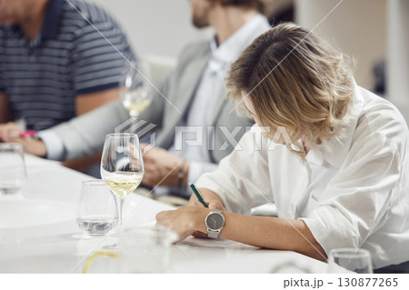 Female member of sommelier school tasting white wine and makes notes in degustation card. Wine expert studies alcoholic drink. Female member of sommelier school tasting white wine and makes notes in degustation card. Wine expert studies alcoholic drink. 130877265