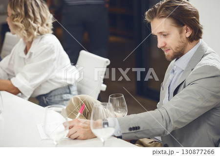 Successful looking male sommelier smelling and tasting white wine into glass during sommelier training.  130877266