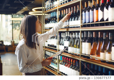 Professional woman sommelier getting wine bottle from shelves, making notes on tablet being at wine cellar. Professional woman sommelier getting wine bottle from shelves, making notes on tablet being at wine cellar. 130877377