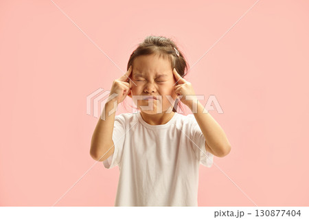 Five year old Japanese appearance Girl Concentrating with Eyes Closed and Fingers on Temples stands over pink isolated 130877404