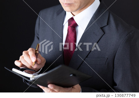 手帳を確認するスーツを着たミドル男性ビジネスマン 130877749
