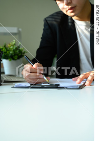 Hands of businessman signing documents on clipboard in office Hands of businessman signing documents on clipboard in office 130879209