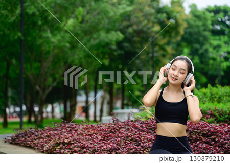 Relaxed female athlete taking a break and listening to music in nature 130879210