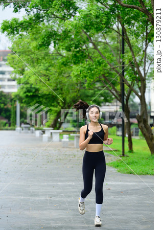 Sporty woman jogging on pathway surrounded by greenery, active lifestyle concept Sporty woman jogging on pathway surrounded by greenery, active lifestyle concept 130879211