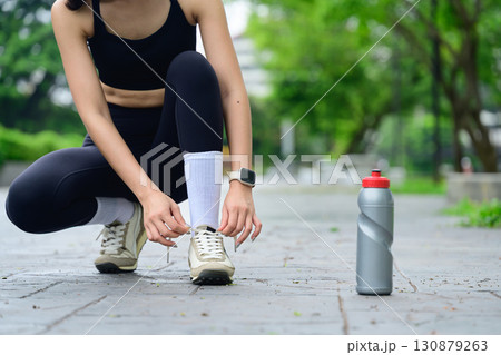 Close up of young woman tying shoelaces before workout with water bottle nearby 130879263