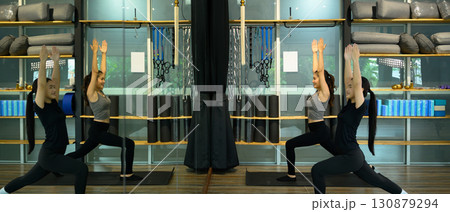 Two women practicing yoga together in a fitness studio, performing a warrior pose 130879294