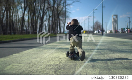 A joyful child happily riding a bright scooter in a sunny park filled with greenery and laughter 130880283