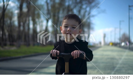 A Joyful Young Child Happily Riding a Colorful Scooter in the Park, Embracing Fun and Adventure 130880297