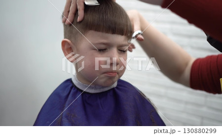 child squinting during haircut at barber 130880299