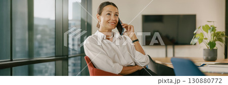 A businesswoman is actively engaging in a productive phone conversation inside her modern office A businesswoman is actively engaging in a productive phone conversation inside her modern office 130880772