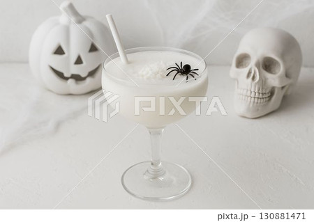 Halloween-themed cocktail with spider decoration beside skull and pumpkin on white background Halloween-themed cocktail with spider decoration beside skull and pumpkin on white background 130881471
