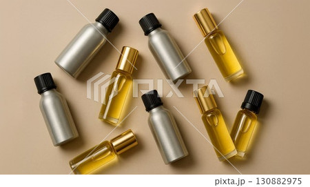 Assorted metallic and glass bottles filled with golden liquid arranged artistically on a soft beige background, showcasing beauty and wellness product packaging design concepts 130882975
