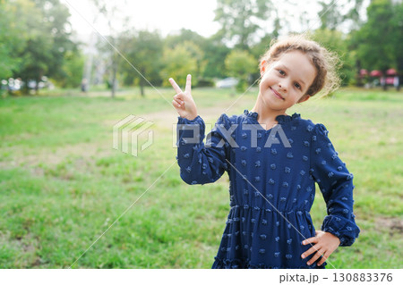 A smiling young girl wearing a navy embroidered dress poses outdoors with a playful peace sign 130883376