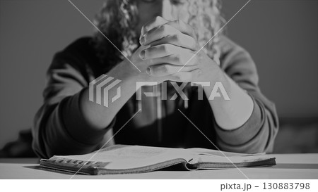 A man with curly hair sits in a worship room, praying intently over a Bible with his palms together. Searching for an answer overcoming a crisis. A scene of faith, solution search, spiritual devotion A man with curly hair sits in a worship room, praying intently over a Bible with his palms together. Searching for an answer overcoming a crisis. A scene of faith, solution search, spiritual devotion 130883798