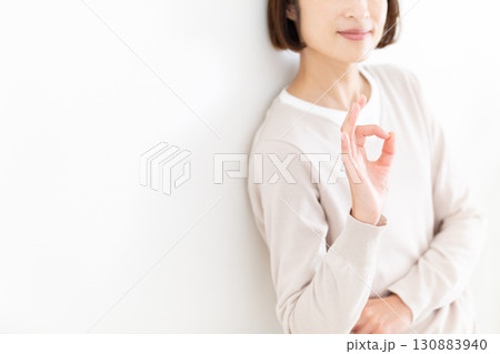 窓際の白壁にもたれて丸サインをするカジュアルのミドル女性 130883940