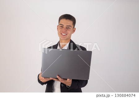The smiling young man in a suit is holding and presenting an open laptop The smiling young man in a suit is holding and presenting an open laptop 130884074