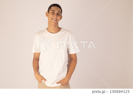 man in a white t-shirt and beidge pants stands with his hands in his pockets  130884125