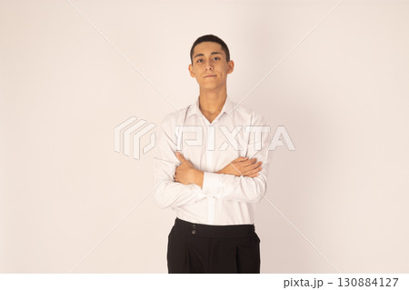 a young man standing with his arms crossed, looking confidently at the camera a young man standing with his arms crossed, looking confidently at the camera 130884127