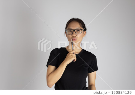 Woman holding a pen to her chin in a thoughtful or questioning pose. Woman holding a pen to her chin in a thoughtful or questioning pose. 130884129