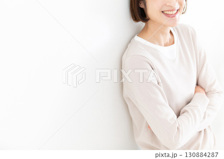 窓際の白壁にもたれて楽しそうに笑うカジュアルのミドル女性 130884287