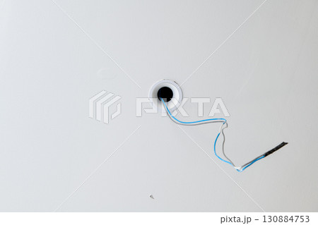 Close up detail of electrical wiring during house construction. renovation project featuring hole in ceiling with blue and black wires ready for light fixture installation Close up detail of electrical wiring during house construction. renovation project featuring hole in ceiling with blue and black wires ready for light fixture installation 130884753