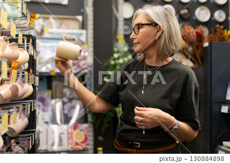 Shopper examines ceramic mug while exploring a home goods store in the afternoon Shopper examines ceramic mug while exploring a home goods store in the afternoon 130884898