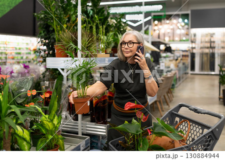 Woman shopping for plants in garden center while talking on the phone near various greenery and 130884944