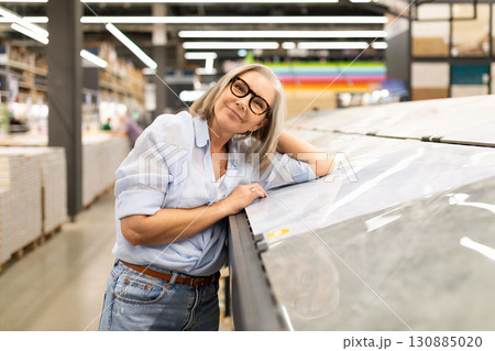 Smiling woman in glasses enjoys browsing materials in a modern home improvement store 130885020