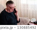 An elderly person utilizes a smartphone while a health monitoring apparatus is placed alongside them, highlighting the embrace of modern conveniences among the older generation 130885492