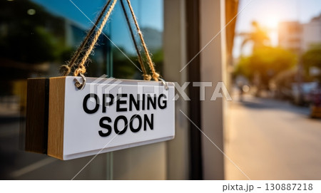 Modern opening soon sign with clean black letters on white board hanging outside glass storefront 130887218
