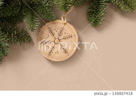 Christmas toy made of decorative wooden slice with ornament snowflake hangs evergreen branches on beige background. Handmade hobby. DIY. Nature material. Xmas decoration. Eco friendly. Zero waste 130887418