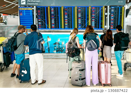 Group of travelers, adorned with backpacks and luggage, stands before an airport departure board, eagerly checking their flight status, a scene capturing the essence of modern travel Group of travelers, adorned with backpacks and luggage, stands before an airport departure board, eagerly checking their flight status, a scene capturing the essence of modern travel 130887422