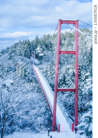 雪化粧した森に架かる、国上山の鮮やかな赤い千眼堂吊り橋 130887616