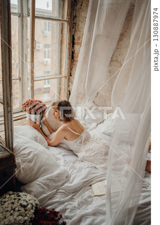 a young blonde woman in a white dress on white sheets 130887974