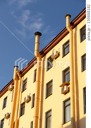 Air conditioners on the facade of a yellow house against a blue sky. An air ventilation. 130888182