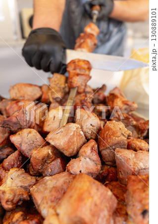 Strong male hands in black rubber gloves removing freshly grilled shish kebab from skewer 130889101