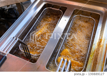 Close-up of deep fryer baskets with sizzling chicken nuggets, onion rings and french fries 130889127