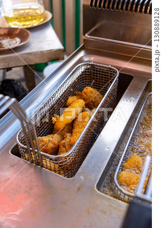 Close-up of deep fryer baskets with sizzling chicken nuggets, onion rings and french fries 130889128