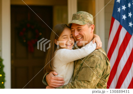 American soldier joyfully embraces his daughter outside their decorated home during holiday festive season. 130889431
