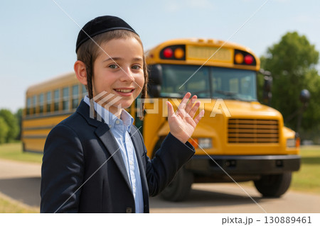 Jewish young boy dressed in traditional clothing smiles waves as school bus prepares to depart in afternoon. 130889461